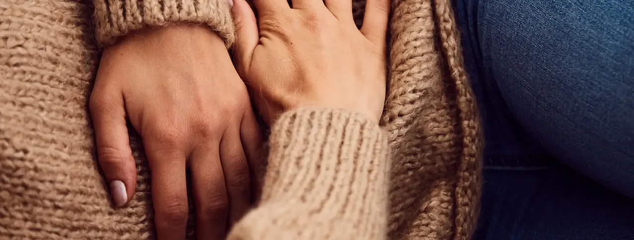 Gros plan sur les mains de deux personnes posées ensemble sur une couverture en tricot beige, dans un geste de soutien - es.